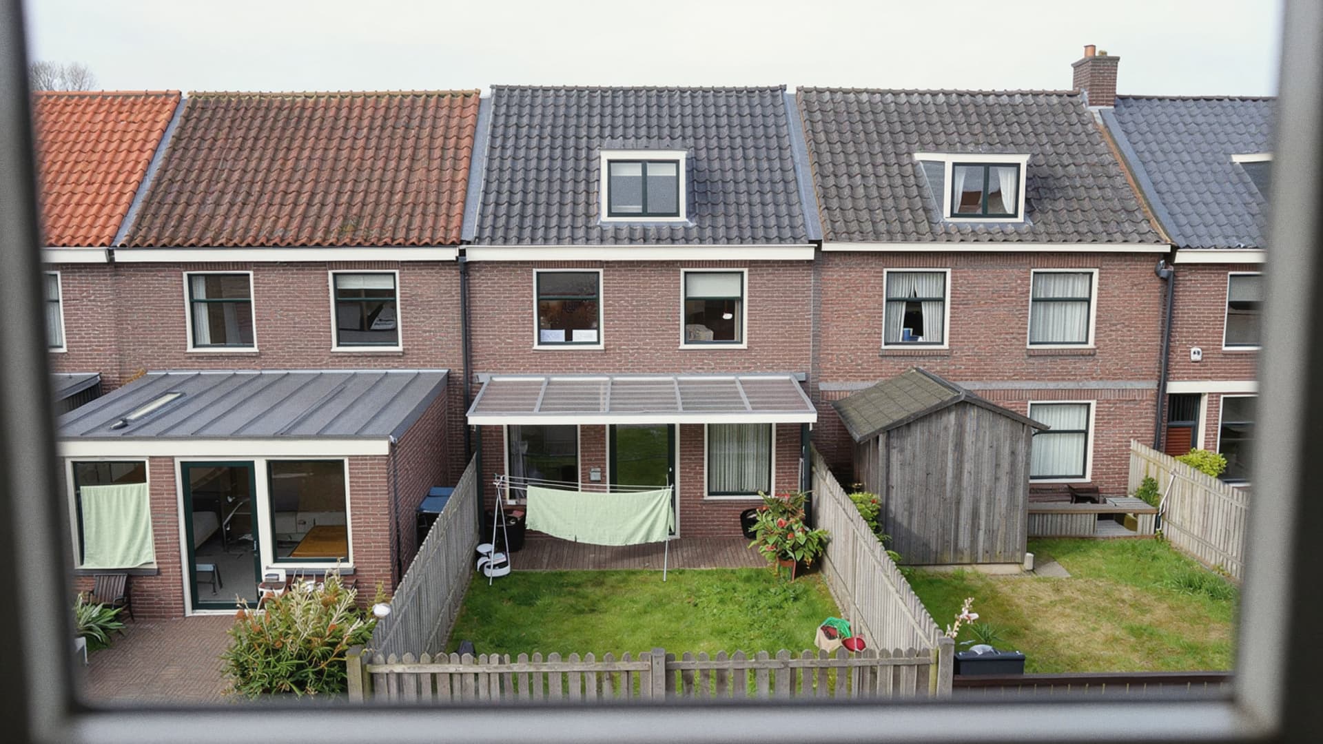 Achterkant van rijtjeshuizen met aanbouwen en smalle tuinen, gezien vanuit een raam boven