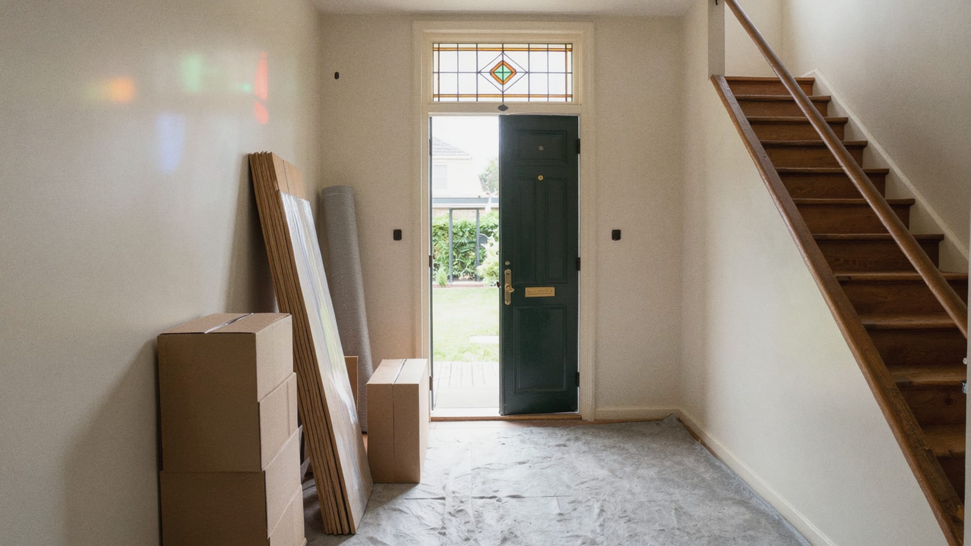Lege gang van een rijtjeshuis met open voordeur, een houten trap en dozen tegen de muur