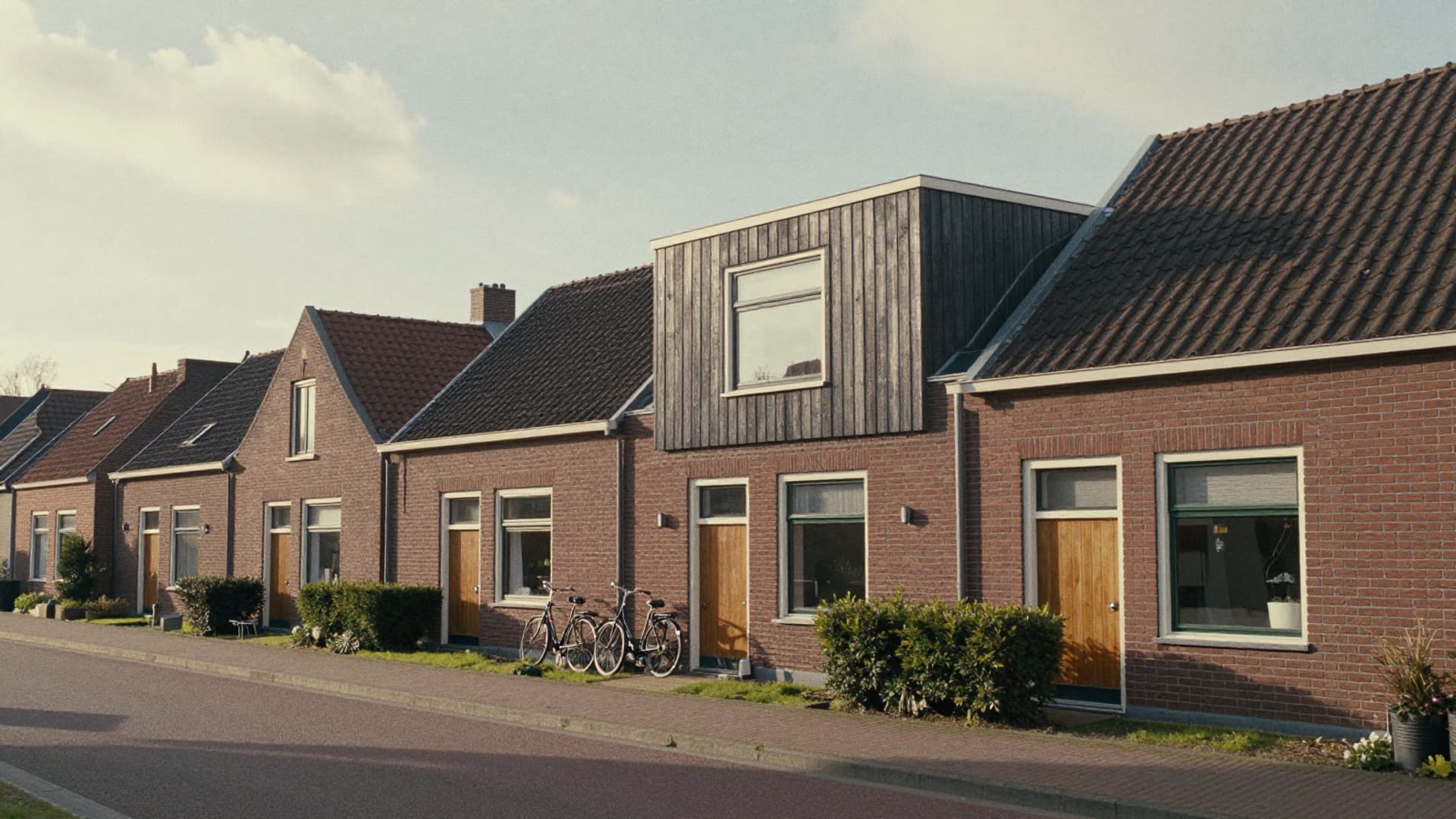 Rij bakstenen rijtjeshuizen, waarvan één een dakopbouw met donkere houten gevelbekleding heeft