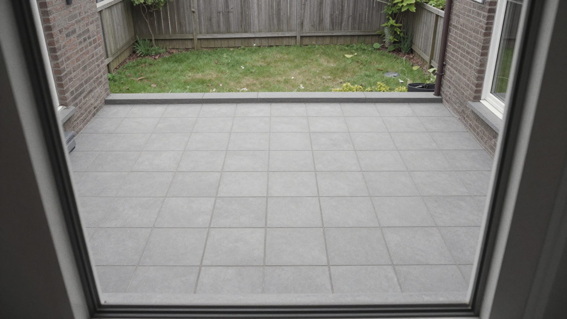 Nieuw terras van grote lichtgrijze keramische tegels in de achtertuin, gezien vanuit het huis
