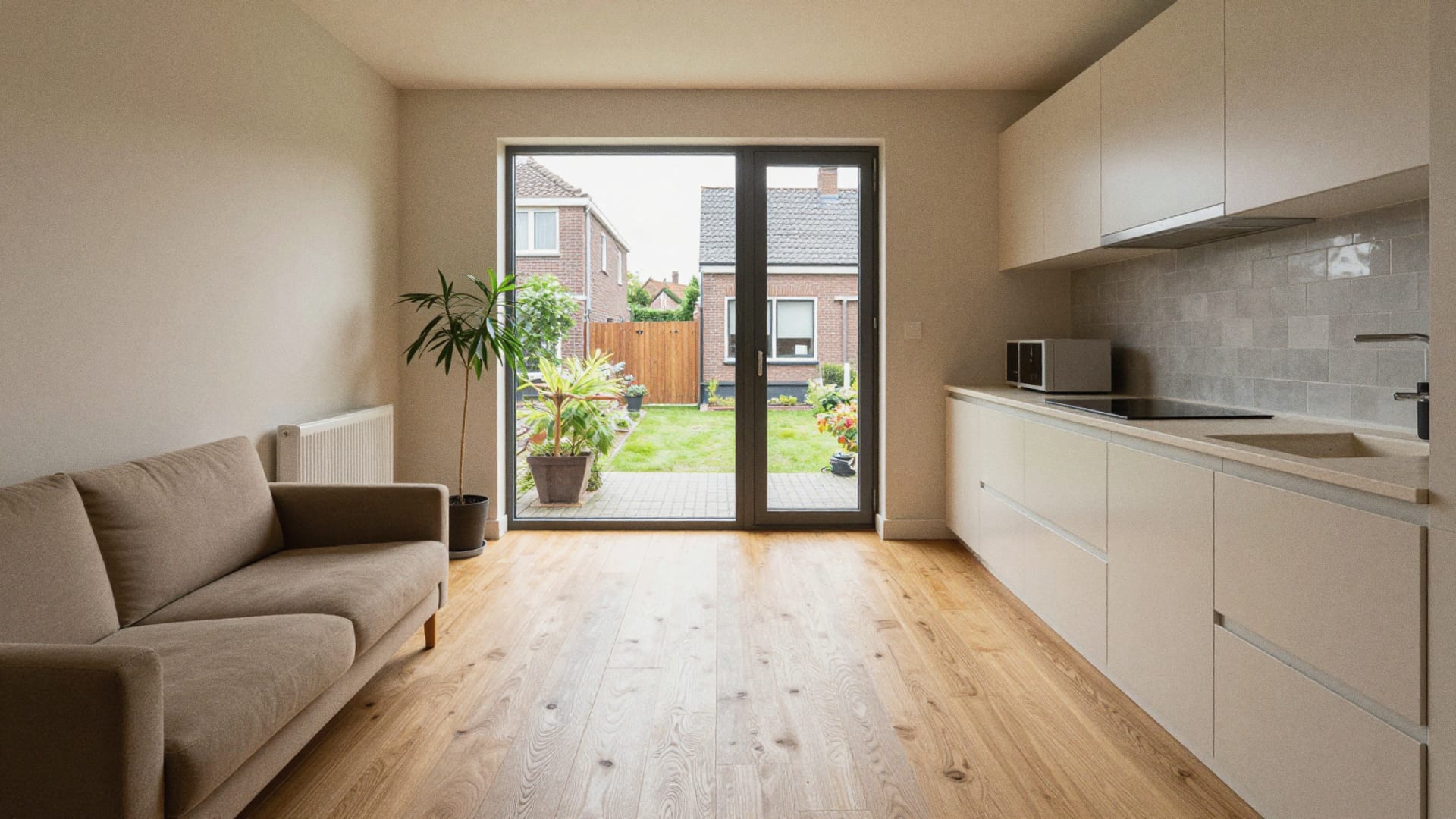 Woonkamer met open keuken en een lichte vloer in houtlook die doorloopt tot de tuindeuren