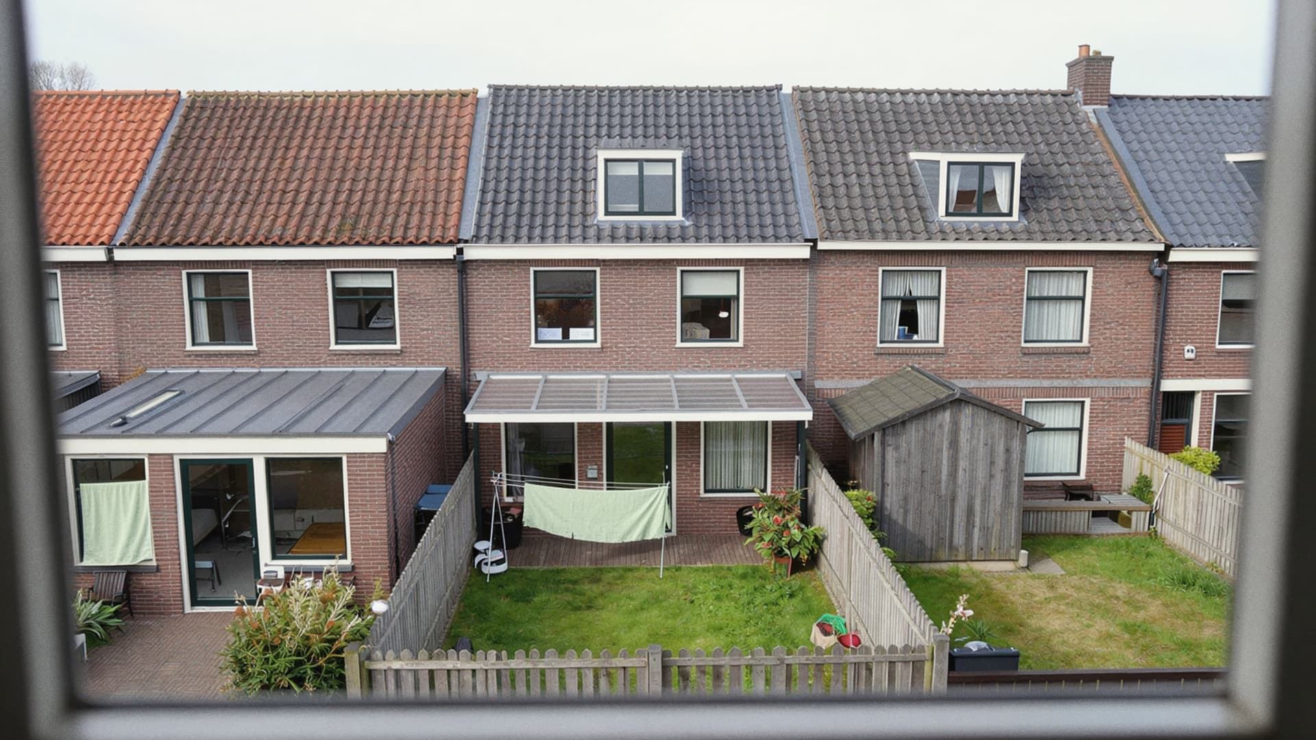 Achterkant van rijtjeshuizen met aanbouwen en smalle tuinen, gezien vanuit een raam boven