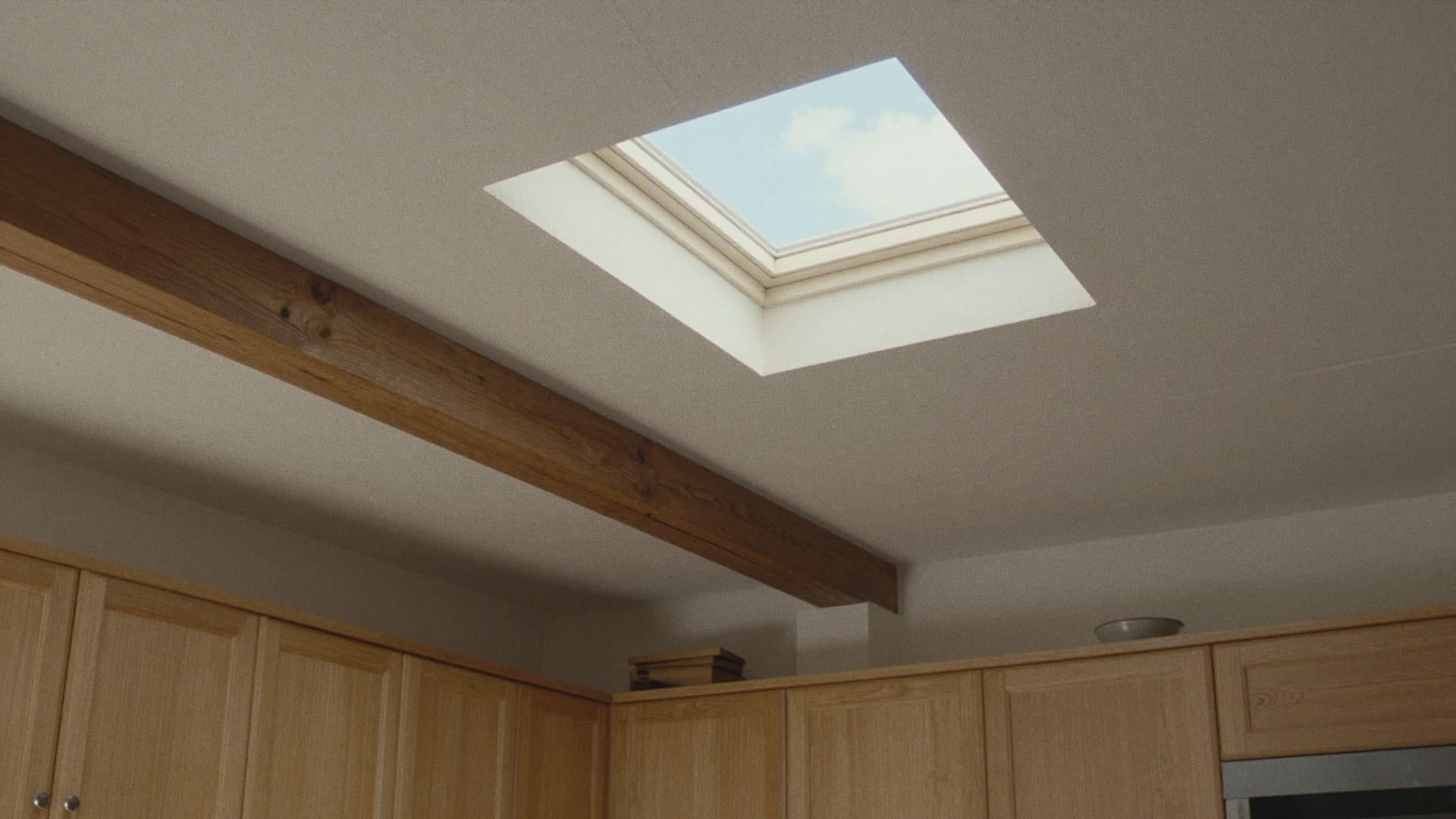 Vierkante lichtkoepel met vlak glas in het plafond van een keuken met eiken kastjes en een houten balk