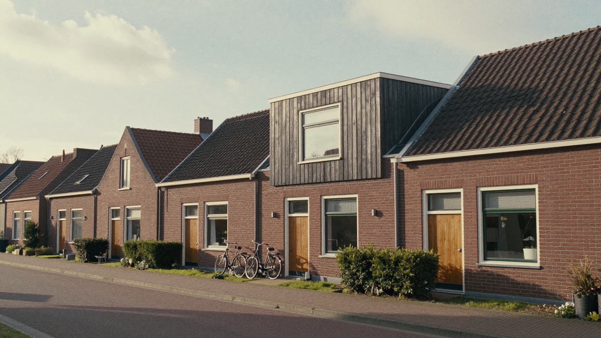 Rij bakstenen rijtjeshuizen, waarvan één een dakopbouw met donkere houten gevelbekleding heeft