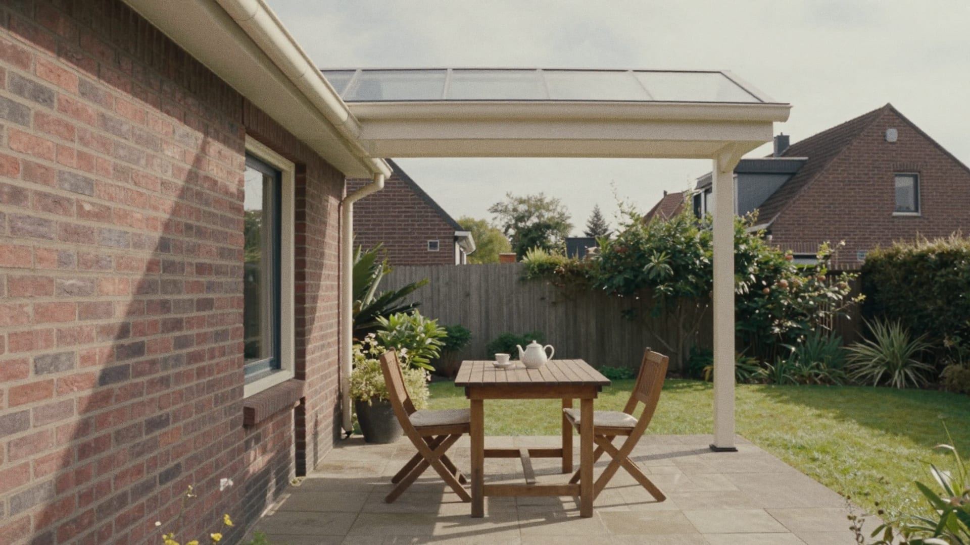 Veranda met een glazen overkapping tegen een bakstenen huis, met een tuintafel en twee stoelen